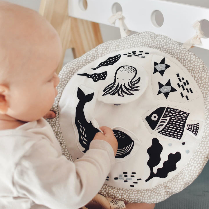 A baby grips the pocket of an ocean animals themed Activity Pad.