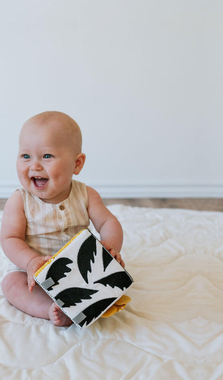 Excited baby sitting on a play mat and holding a black and white soft block activity.