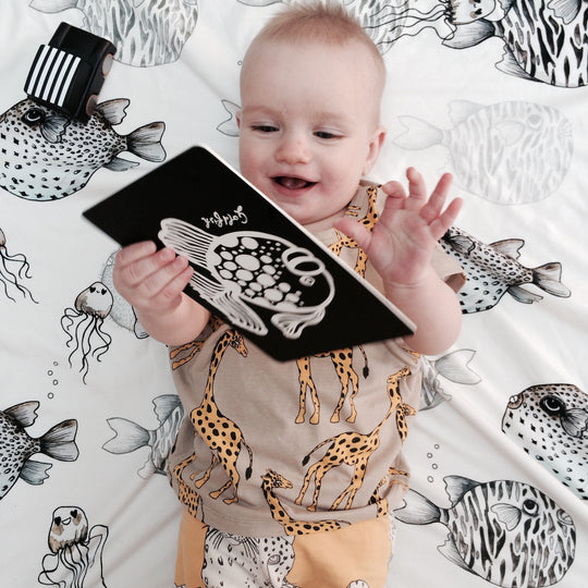 Baby smiling holding a black and white illustrated fish Art Card.