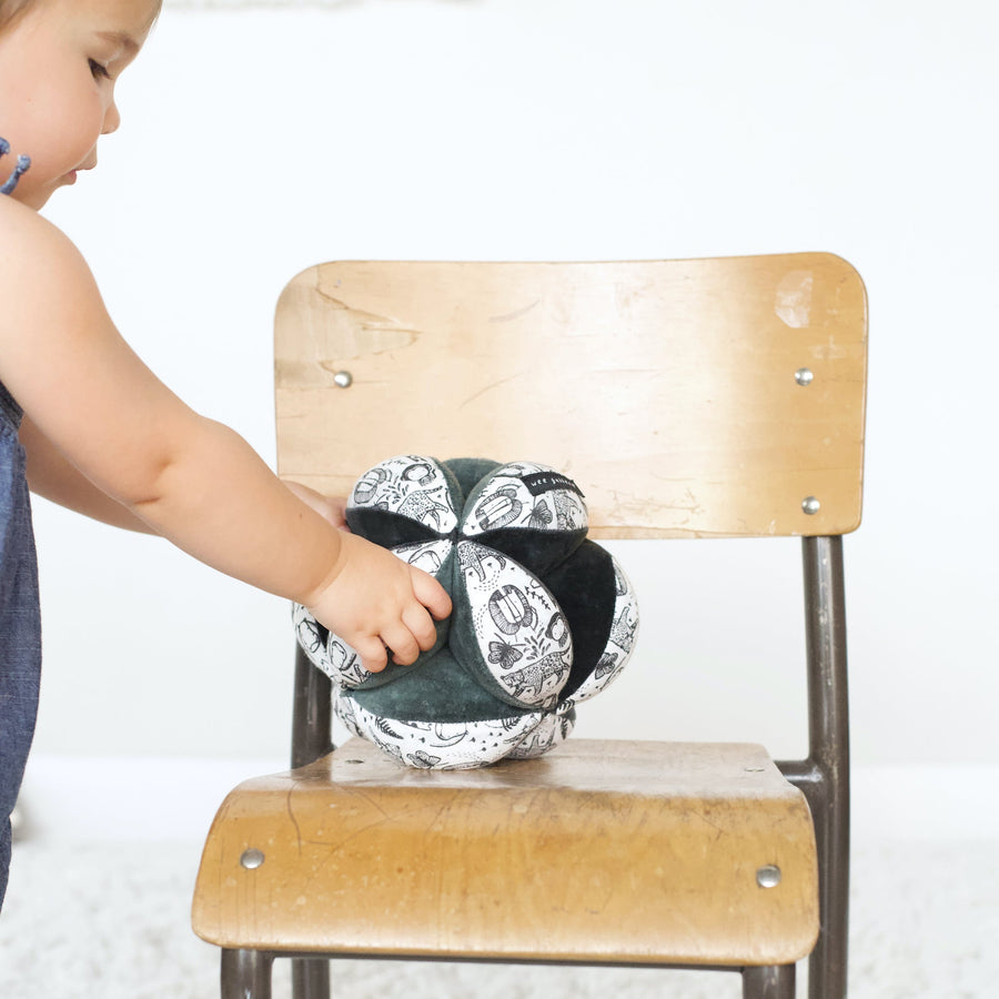 toddler girl reaching for clutch ball on small chair