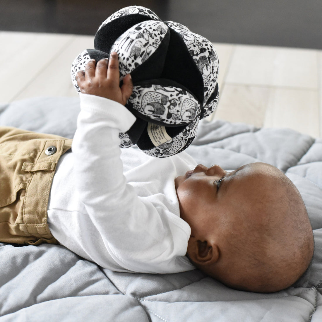 baby boy laying and holding ball up to gaze at its black and white pattern